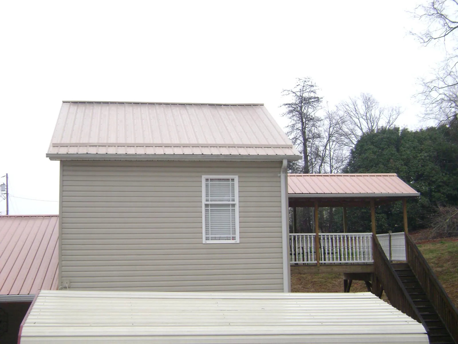 Tan metal roofs on a two story addition and attached porch, from a Roof Replacement job in Williams
